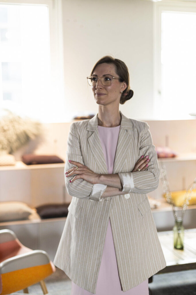 Ich-bin-nicht-gescheitert Janine Frank steht in einem hellen Büro, schaut nach links und wirkt gedankenverloren.