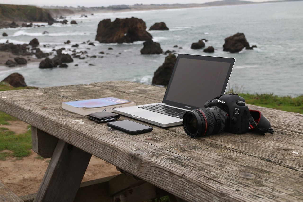 Nebeneinkommen als Fotografin Laptop und Fotoapparat stehen auf einem Tisch am Meer